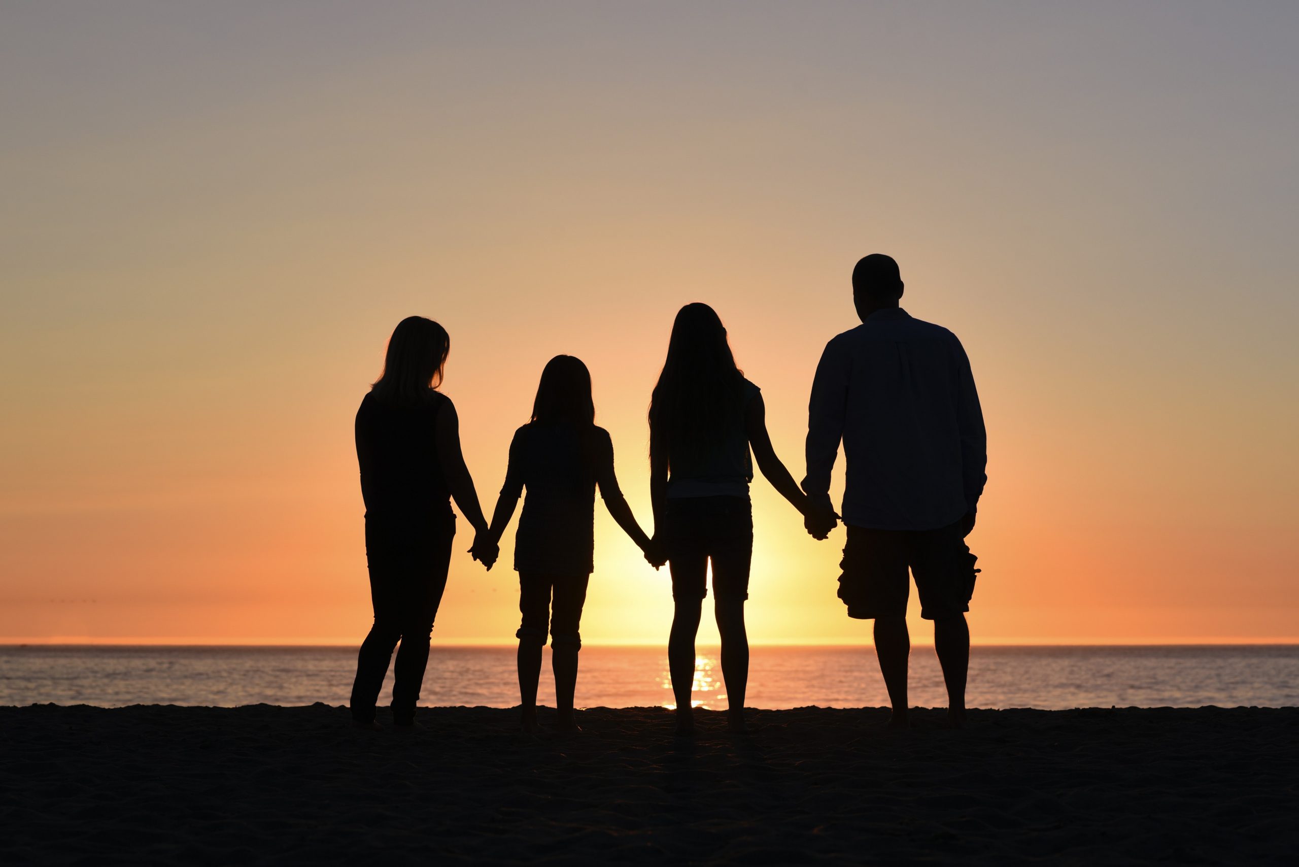 sunset silhouette of family of four looking at beach